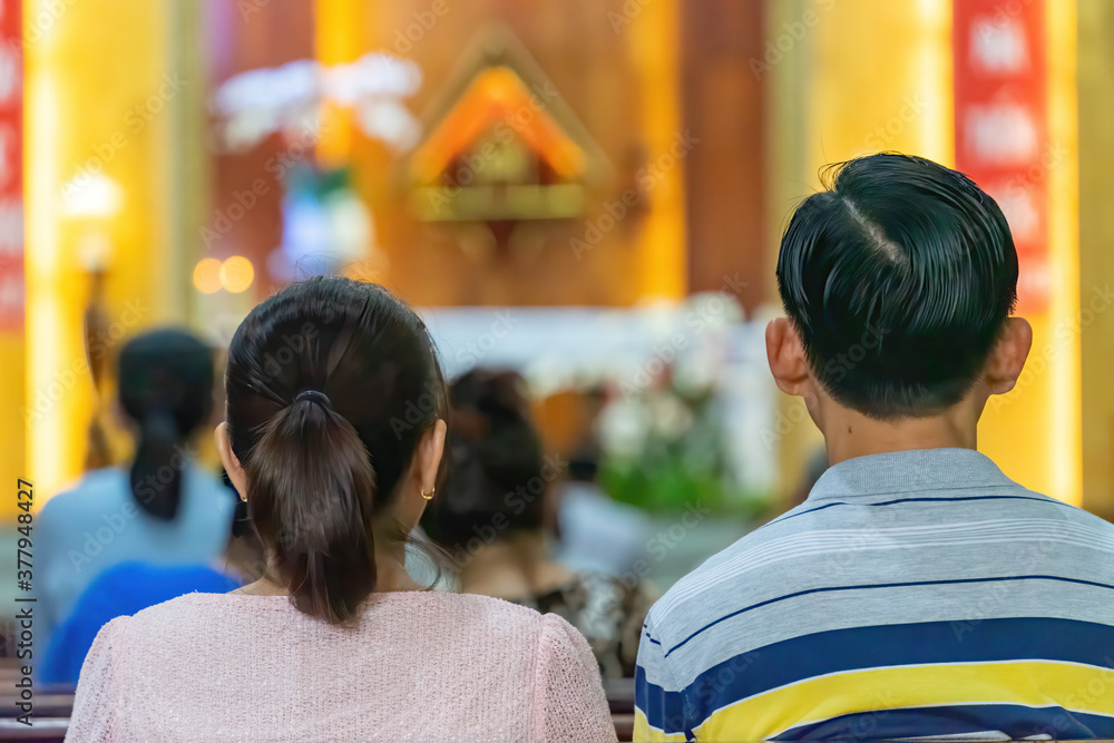 A blurred background photo of the inside of a Vietnamese church sanctuary that is filled with people in the pews, and the pastor stands under a large cross at the altar, in Vietnam. A blurred background photo of the inside of a Vietnamese church sanctuary that is filled with people in the pews, and the pastor stands under a large cross at the altar, in Vietnam.