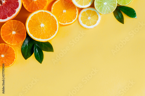 Slices of citruses are laid out in gradient composition in upper left corner of background. Tangerines, oranges, grapefruits, lemons, limes are lying on yellow canvas. Summer exotic tropical fruits.