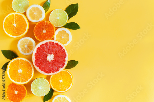 Slices of citruses are laid out in composition in left side of background. Pieces of tangerines, oranges, grapefruits, lemons, limes are lying on yellow canvas. Summer exotic tropical fruits.