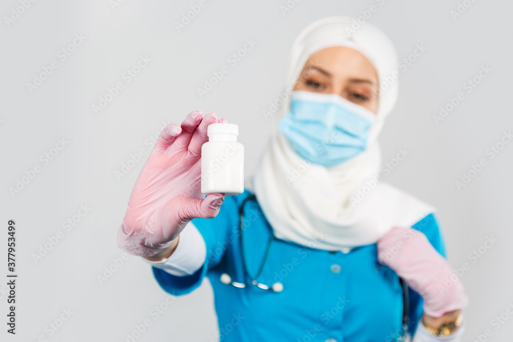friendly Muslim doctor or nurse in a hijab, mask, gloves offering a pill to the patient on a gray background friendly Muslim doctor or nurse in a hijab, mask, gloves offering a pill to the patient on a gray background