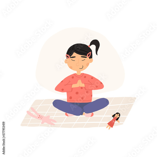 Cute Asian girl put down a toys and meditates in lotus or padmasana pose with her hands folded at the heart.