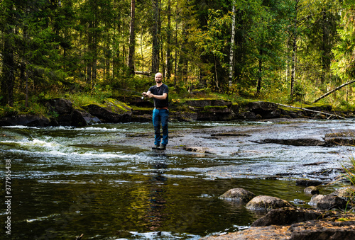 Male hiker fishing in a stream running through a wild forest.