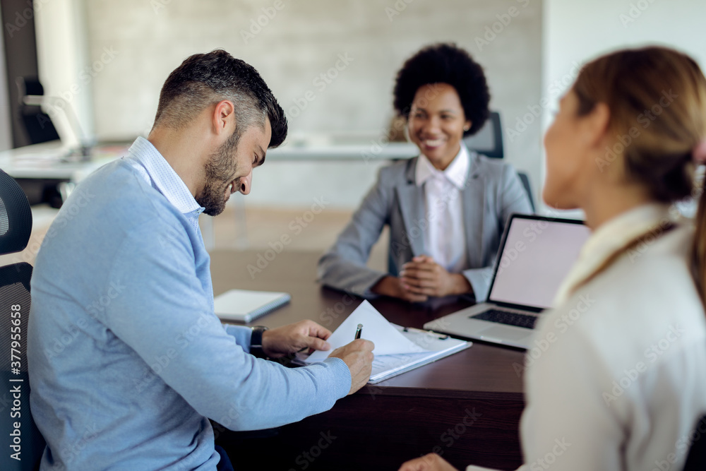 Happy man signing an agreement while being with his wife on a meeting with financial advisor. Happy man signing an agreement while being with his wife on a meeting with financial advisor.