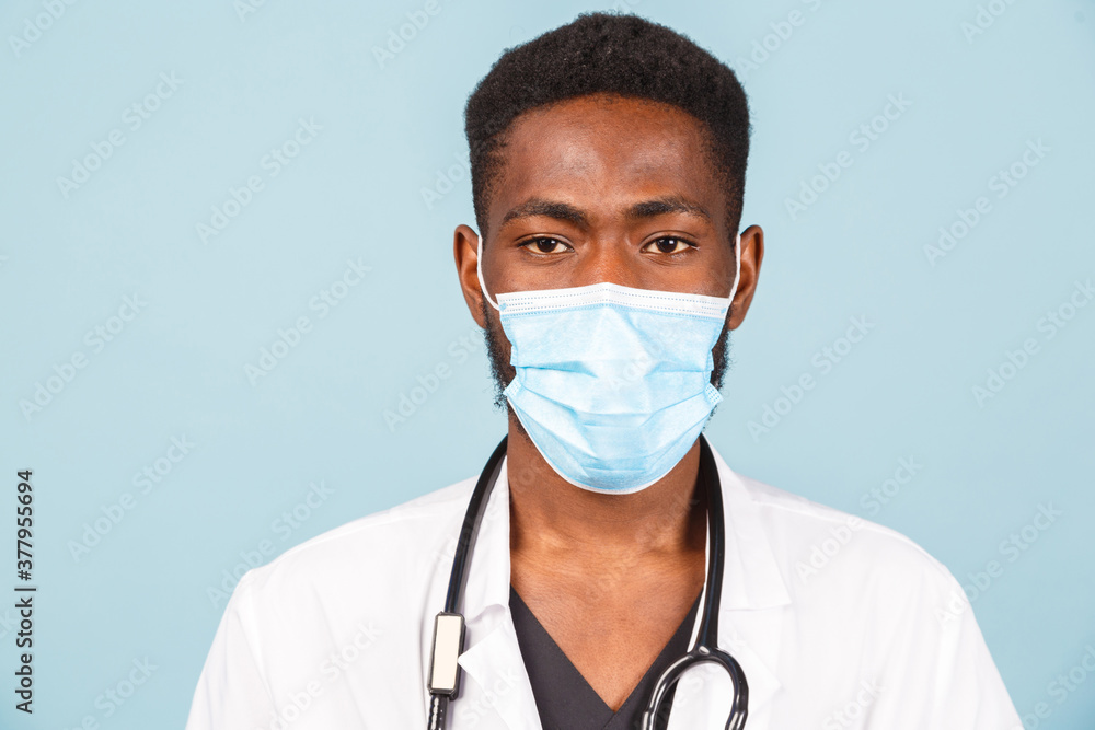 African American male doctor with stethoscope in mask over blue background. African American male doctor with stethoscope in mask over blue background.