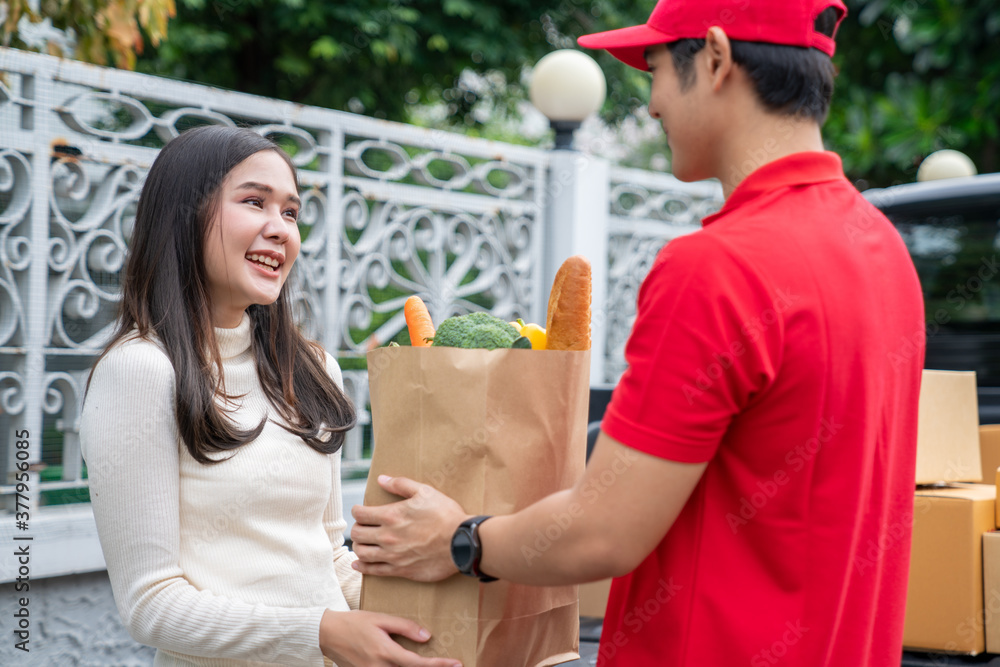 Selective Focus of smiling woman receiving a grocery bag from the courier. A delivery man bringing fresh food packages to customer on a business day. Online shopping, food delivery service concept.