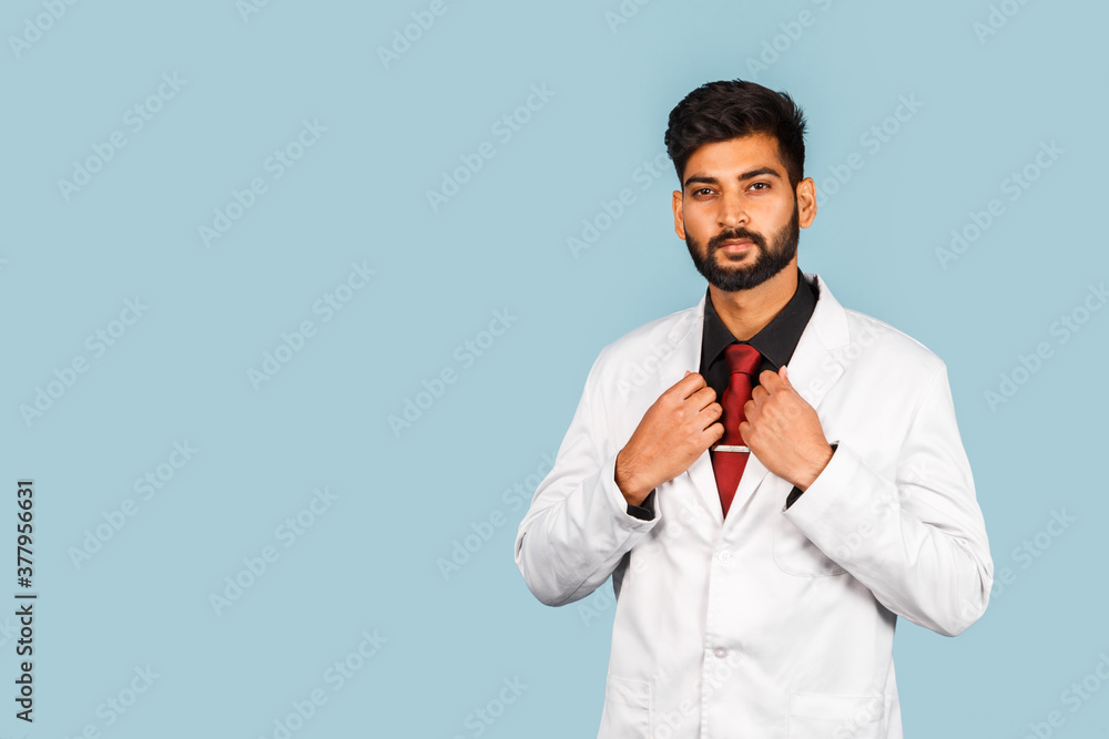 Handsome modern indian / asian doctor with stethoscope, tie and white coat on blue background Handsome modern indian / asian doctor with stethoscope, tie and white coat on blue background