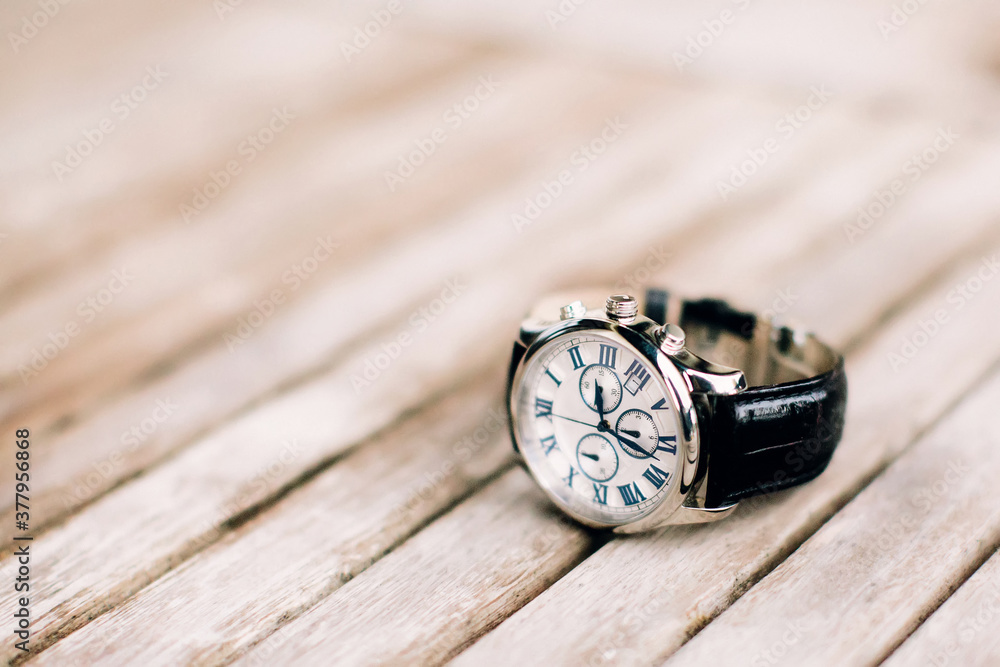 Men's wrist watch with black strap lies on wooden surface. Selective focus. Men's wrist watch with black strap lies on wooden surface. Selective focus.