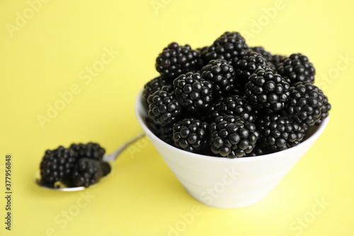 Fresh ripe blackberries in bowl on yellow background