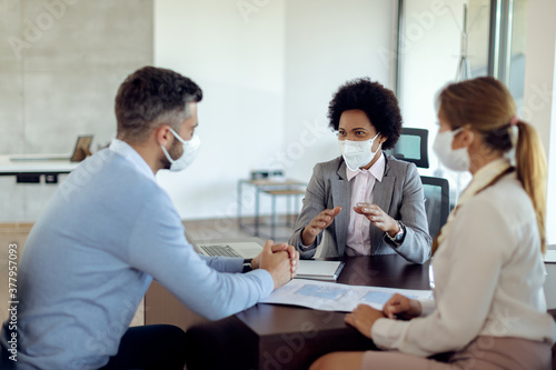 African American insurance agent with a face mask talking to her clients on a meeting in the office.