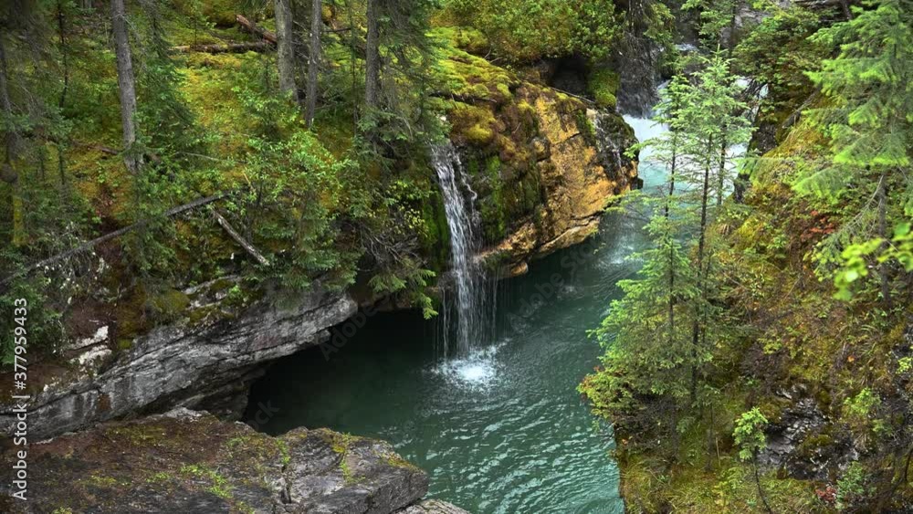 Small waterfall drops into a green clear stream with a larger waterfall in the background. The setting is a lush green forest and rock ledges.
Small waterfall drops into a green clear stream with a larger waterfall in the background. The setting is a lush green forest and rock ledges.