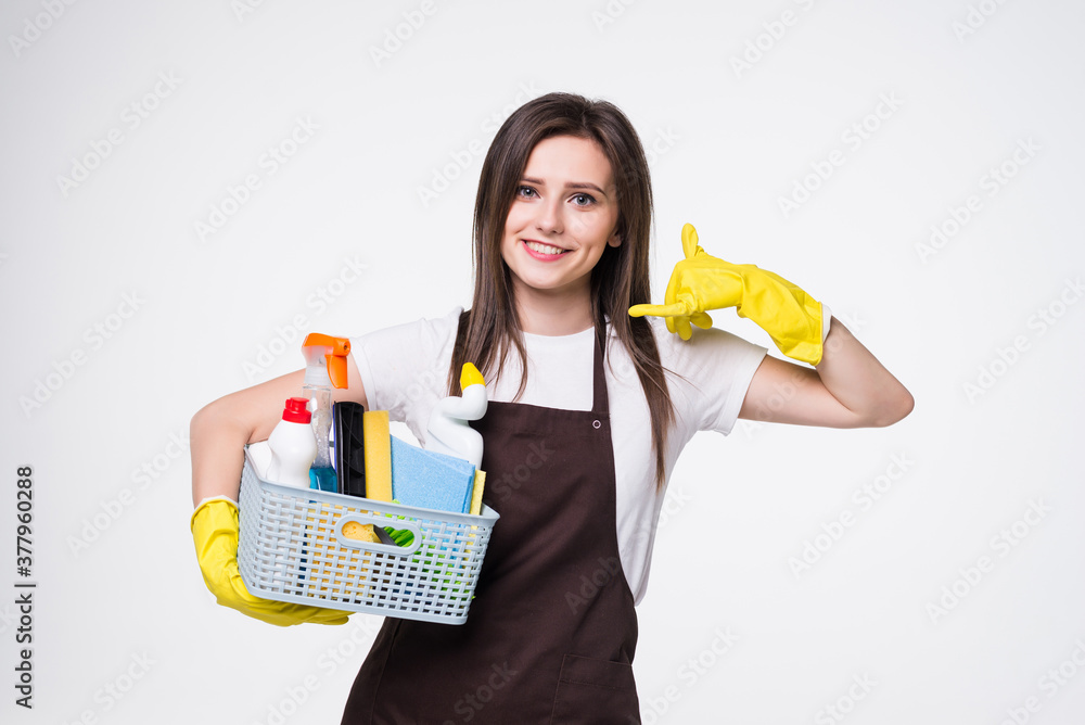 Pretty young woman holding red bucket of cleaning products with call me back gesture isolated on white background. House cleaning concept Pretty young woman holding red bucket of cleaning products with call me back gesture isolated on white background. House cleaning concept