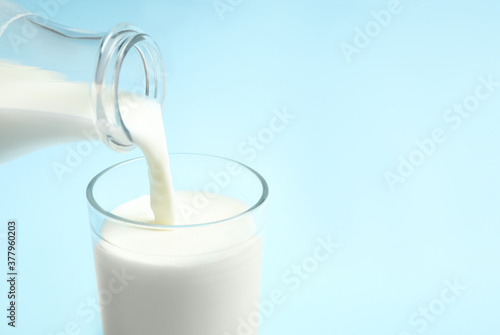 Pouring milk into glass on light blue background, closeup. Space for text
