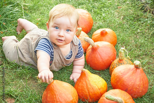 Infant smiling little caucasian and orange pumpkins on a background of green grass