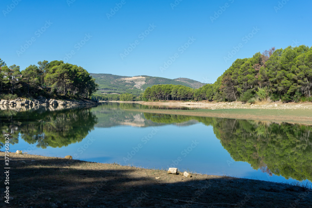 Reservoir landscape with nice reflections of the forest in the water on a day with blue sky