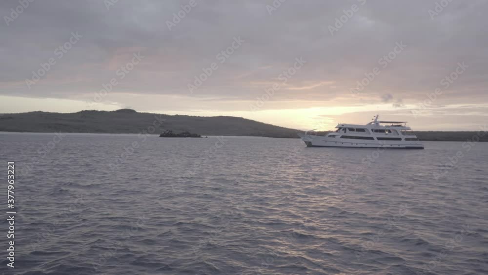 A white yacht or cruise is anchored during sunset close to an island of the Galapagos islands. The ocean has some current. A white yacht or cruise is anchored during sunset close to an island of the Galapagos islands. The ocean has some current.