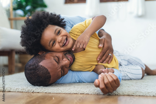 Fotografija Black father in living room have a fun playing together on warm floor at home