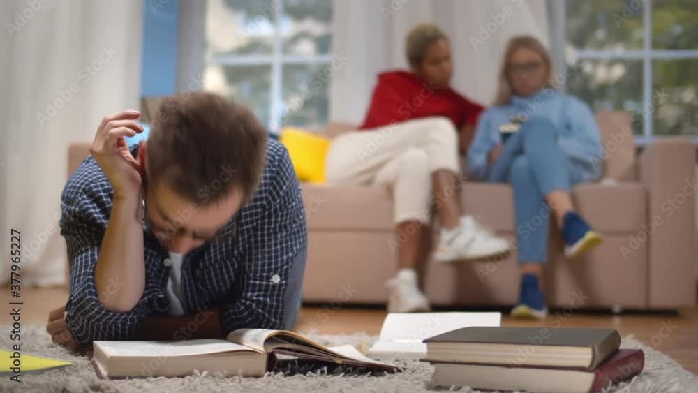 Tired student sleeping over open book lying on floor in shared living room