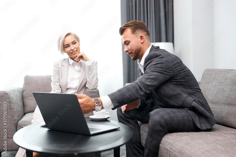 confident guy show at laptop to female business partner, business colleagues at meeting, sit on sofa and talk confident guy show at laptop to female business partner, business colleagues at meeting, sit on sofa and talk