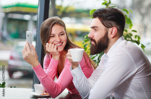 Happy and loving couple in cafe with smartphone, having fun communicating