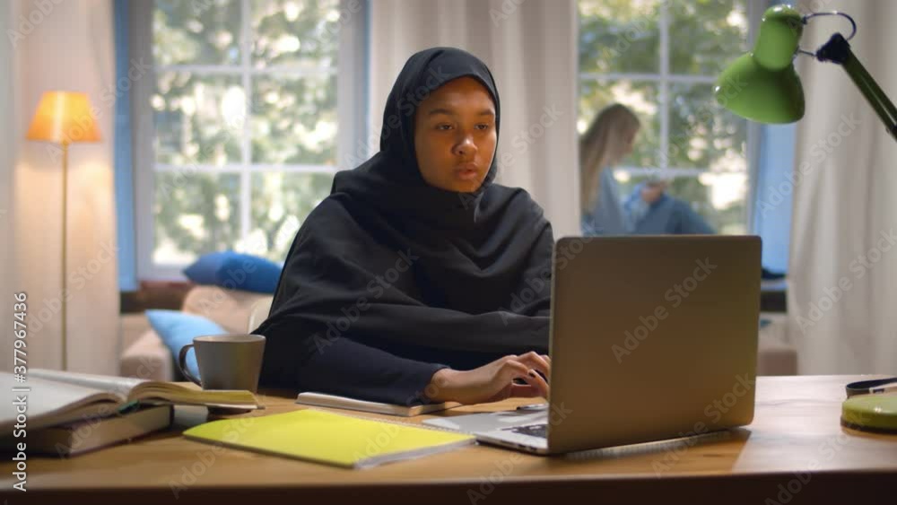 Islamic young woman student wearing abaya and typing on laptop in college common room Islamic young woman student wearing abaya and typing on laptop in college common room