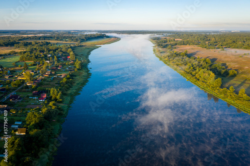Beautiful aerial view of the Volkhov river in Russia. Early morning landscape. Foggy river. River valley in the morning fog at sunrise. View from above.