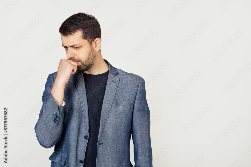 Male businessman with a beard, looks tense and nervous with his hands on his mouth biting his nails. Anxiety problem. Portrait of a man on a gray background Male businessman with a beard, looks tense and nervous with his hands on his mouth biting his nails. Anxiety problem. Portrait of a man on a gray background