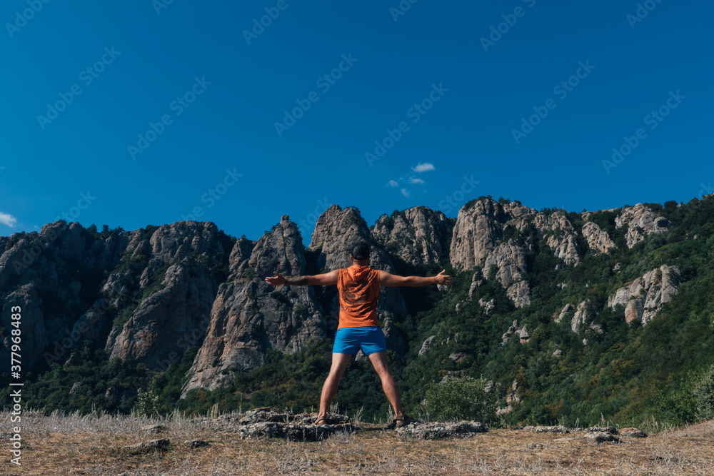A man tourist stands on a rock against the backdrop of a cliff and mountains