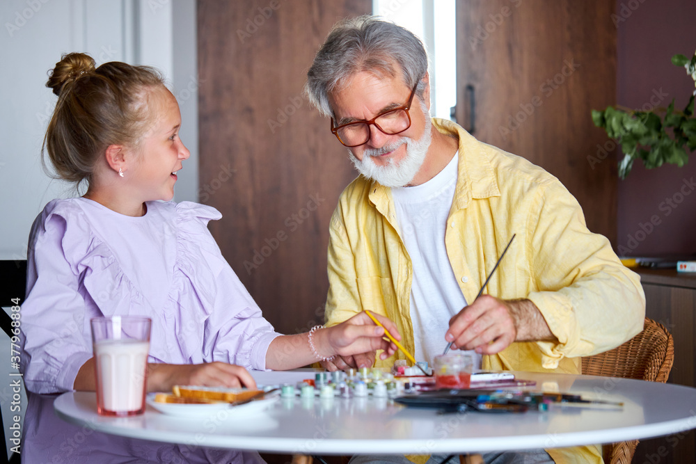 senior grandfather teach little girl to draw, help to develop creativity, they use paints and brushes senior grandfather teach little girl to draw, help to develop creativity, they use paints and brushes