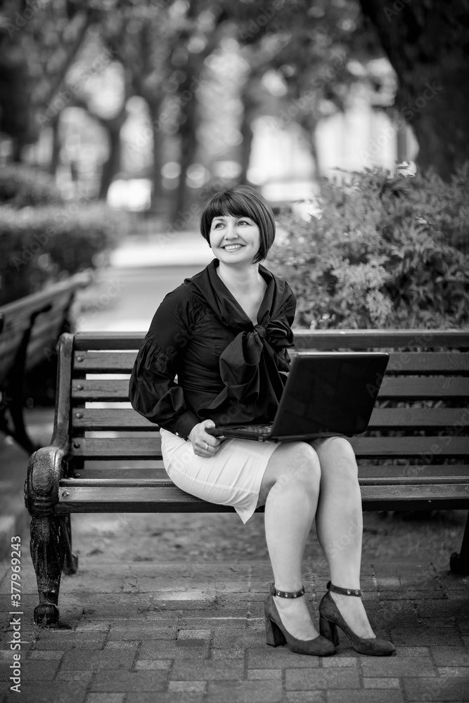 black and white portrait of a woman in business style, with a laptop, on a bench in the Park, working remotely in the field of Economics and accounting. black and white portrait of a woman in business style, with a laptop, on a bench in the Park, working remotely in the field of Economics and accounting.