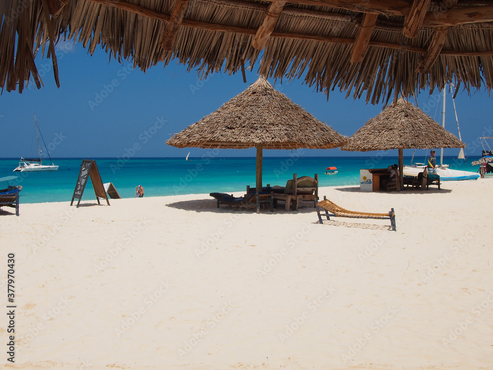 Zanzibar island, Tanzania - 08/15/2020: Sunny beach day, white sand, blue Indian ocean and  sun umbrellas. Copy space for text.