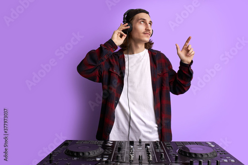 young caucasian dj man perform music with the use of special equipment, long haired male in casual wear have fun, wearing headphones. music, dj concept. studio shoot