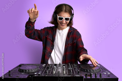 positive male DJ playing music on purple background, caucasian long haired man in casual wear perform club music, wearing headphones