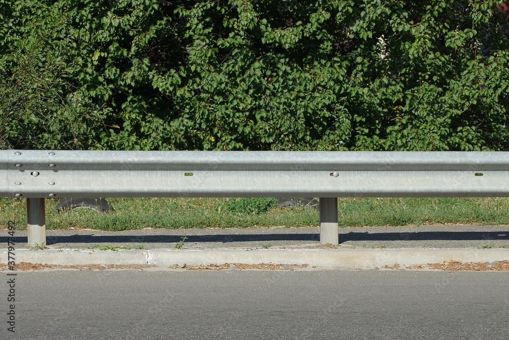 long gray metal barrier bump along the paved road in front of green vegetation long gray metal barrier bump along the paved road in front of green vegetation