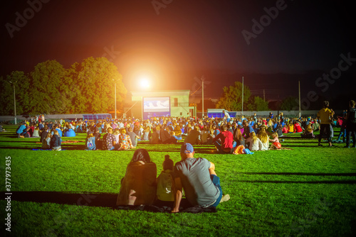 Summer cinema. People and couples watching a movie on the screen of a summer cinema in the evening