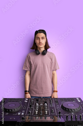 portrait of serious confident man in cap and headphones standing next to dj console, look at camera. before party. disco dance