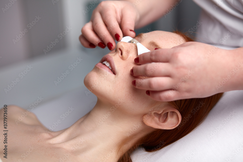 redhead young woman getting facial care by beautician in salon, facial peeling. skin care, beauty concept redhead young woman getting facial care by beautician in salon, facial peeling. skin care, beauty concept