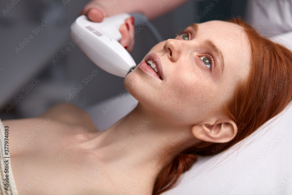Naklejka premium cosmetologist doing photo rejuvenation procedure for woman patient, beautiful lady lie enjoying beauty procedures, want soft healthy skin