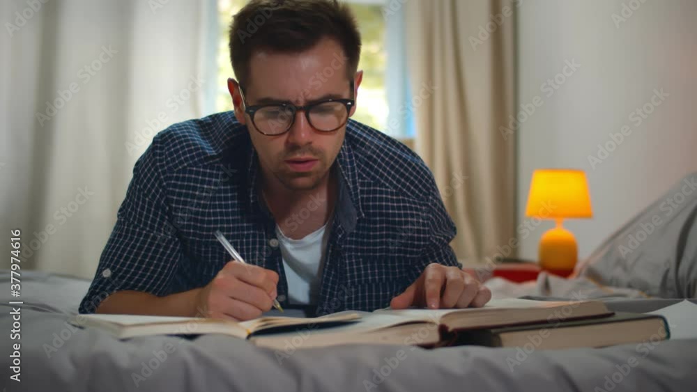 College student lying on bed at home and writing in copybook and reading books when doing homework College student lying on bed at home and writing in copybook and reading books when doing homework