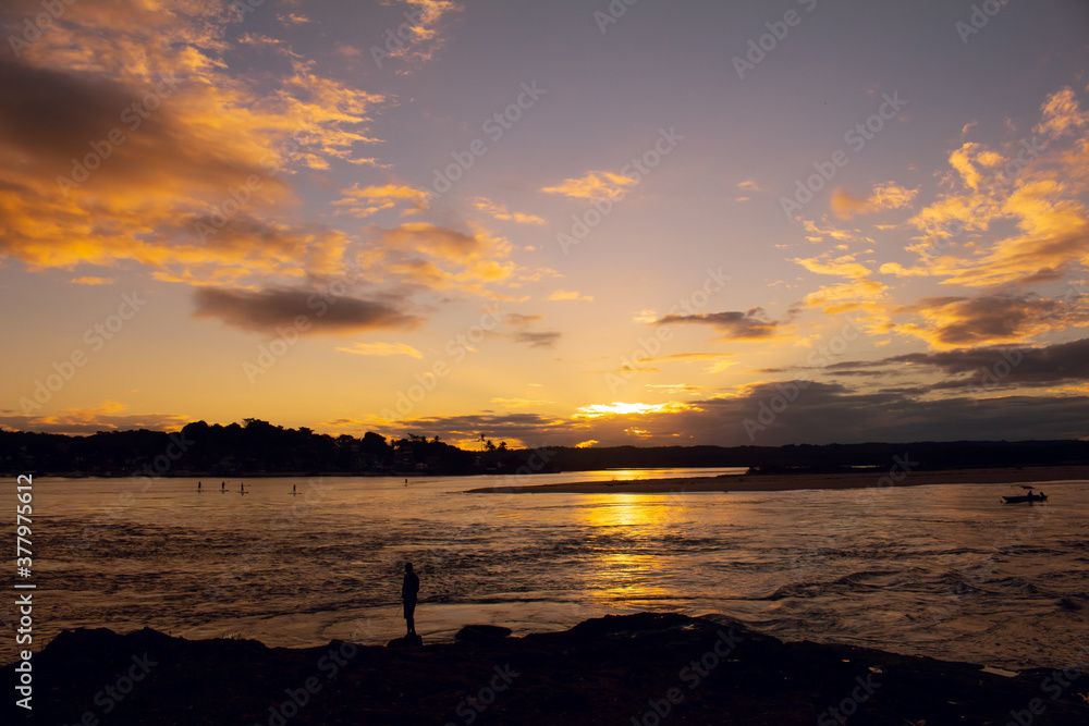 Beautiful sunset on the edge of the river. A fisherman on the coast looking for food. The sky full of golden colored lights.