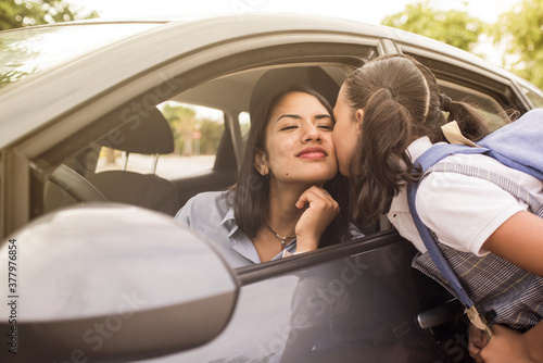 School girl kisses her mother before entering class. Young mother in the car, leaving her daughter at school.
