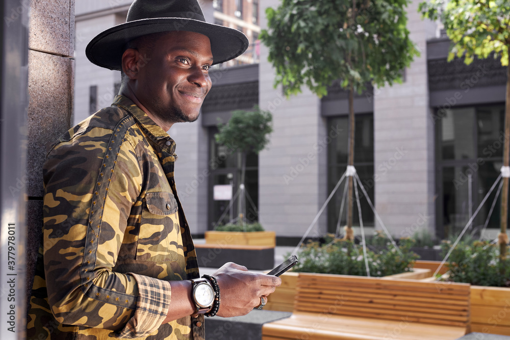 fashionable african man hold mobile phone in hands outdoors, chatting with someone or surfing the Net fashionable african man hold mobile phone in hands outdoors, chatting with someone or surfing the Net