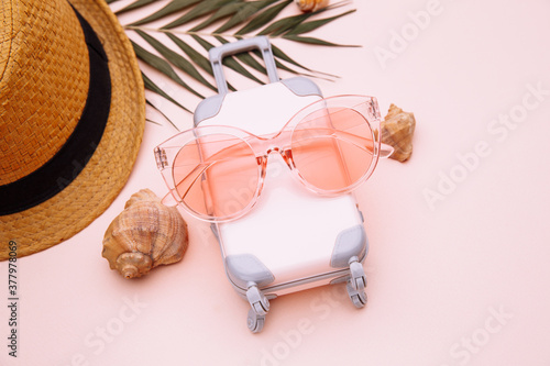 Pink suitcase and summer accessories on pink background close-up. Travel, summer vacation or tourism concept.