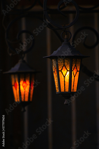 two hanging iron black lanterns with frosted glasses burning in the dark of the night