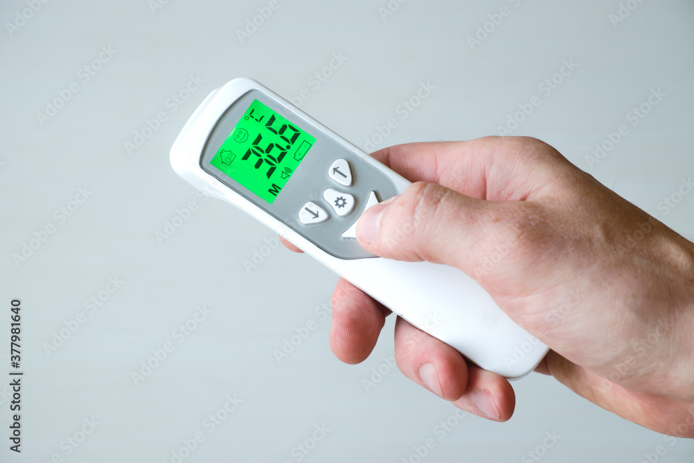 Hand holding contactless thermometer, showing temperature 36.6 degrees by Celsius on white background. Temperature measurement. Hand holding contactless thermometer, showing temperature 36.6 degrees by Celsius on white background. Temperature measurement.