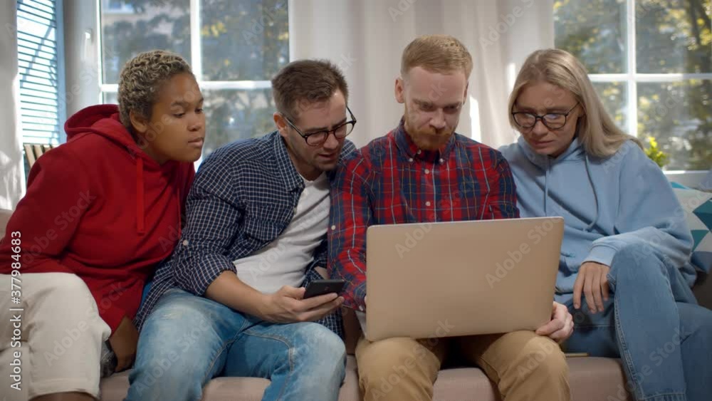 Group of friends enjoying time together and looking at laptop sitting on couch Group of friends enjoying time together and looking at laptop sitting on couch