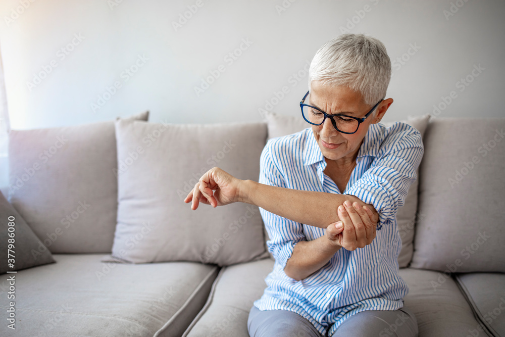 © Dragana Gordic - Senior woman with arm pain.Old female massaging painful hand indoors. Old woman hand holding her elbow suffering from elbow pain. Senior woman suffering from pain in hand at home.