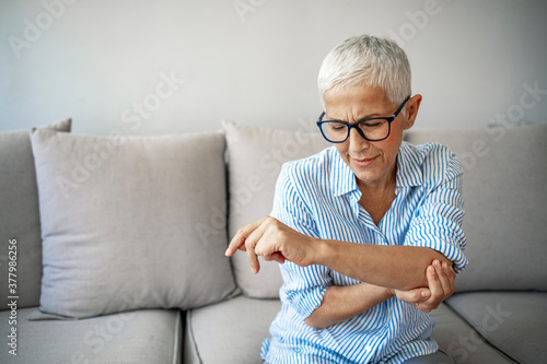 Elbow Pain In An Elderly Person. People, health care and problem concept - unhappy woman suffering. Senior woman suffering from pain in hand at home. Mature woman suffering from elbow pain at home photo