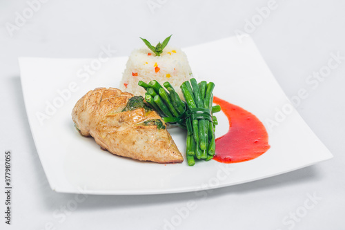 Pan roasted chicken breast with long green beans and light vegetable rice platter. Food decorating with red sauce on a white plate. Isolated white background.