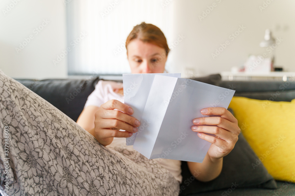 Low angle view on caucasian woman sitting at home on the sofa bed opening envelope with letter in day - Leisure activity receiving contract greeting card or invoice concept Low angle view on caucasian woman sitting at home on the sofa bed opening envelope with letter in day - Leisure activity receiving contract greeting card or invoice concept