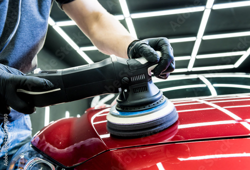 Car service worker polishes a car details with orbital polisher.